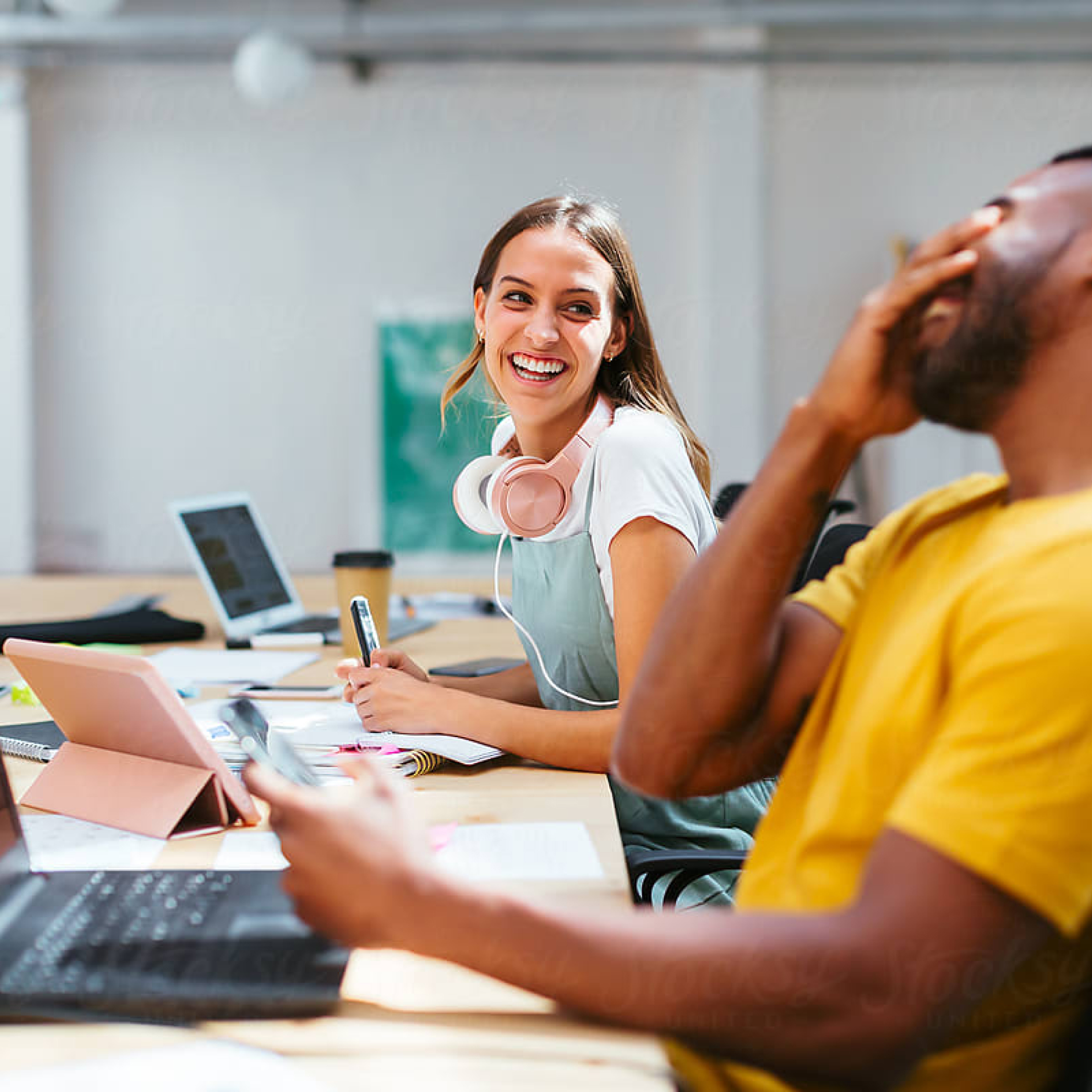 Woman with headphones around her neck who uses Carbonite auto backup smiles at a person sitting beside her.